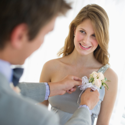 A guy pinning a corsage on his date for the dance. Credit: Tetra Images on gettyimages.com