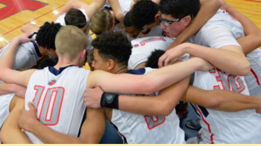 The mens varsity basketball team in a group huddle.