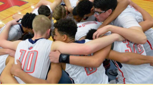 The men's varsity basketball team in a group huddle.