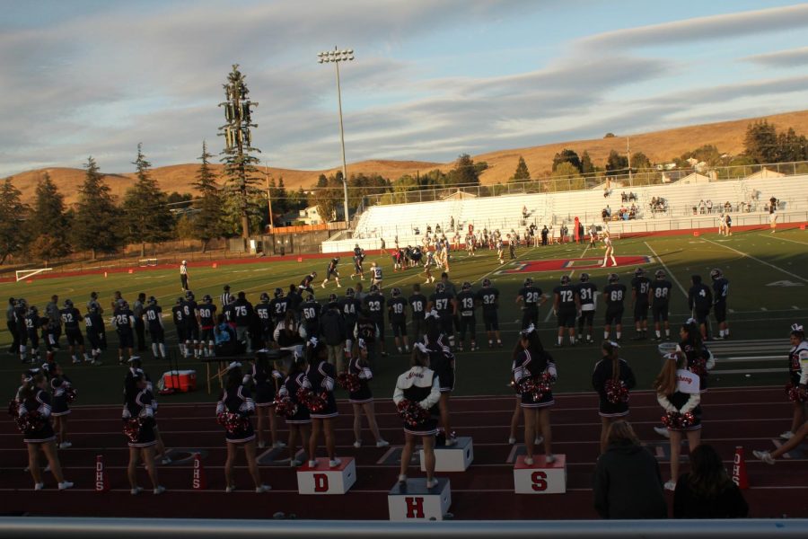 The+varsity+football+team+and+the+varsity+sideline+cheerleaders+stand+for+the+national+anthem.